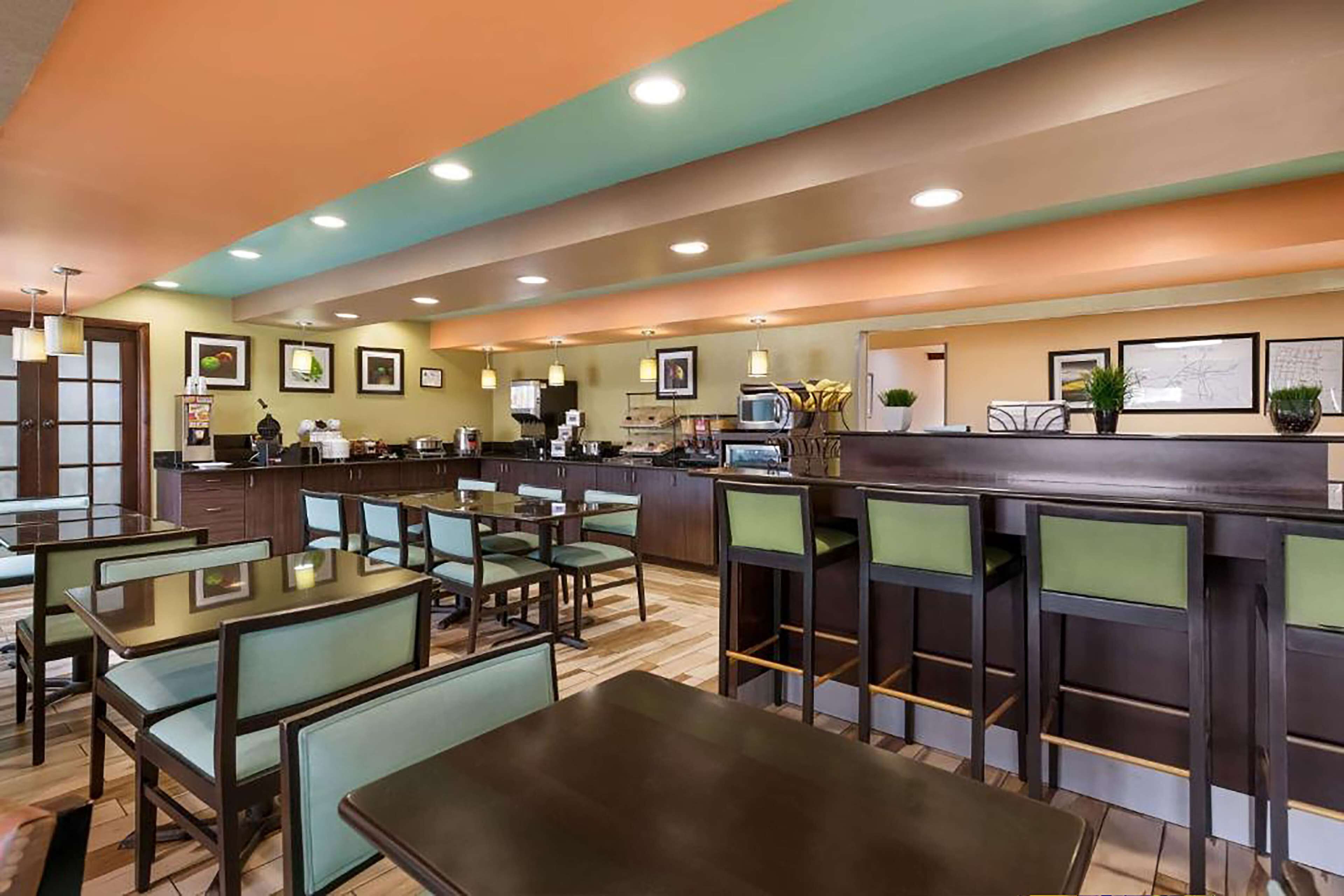 Un restaurante con zona de bar, distintas opciones de asientos, incluyendo cabinas y mesas altas, y una cocina visible al fondo.