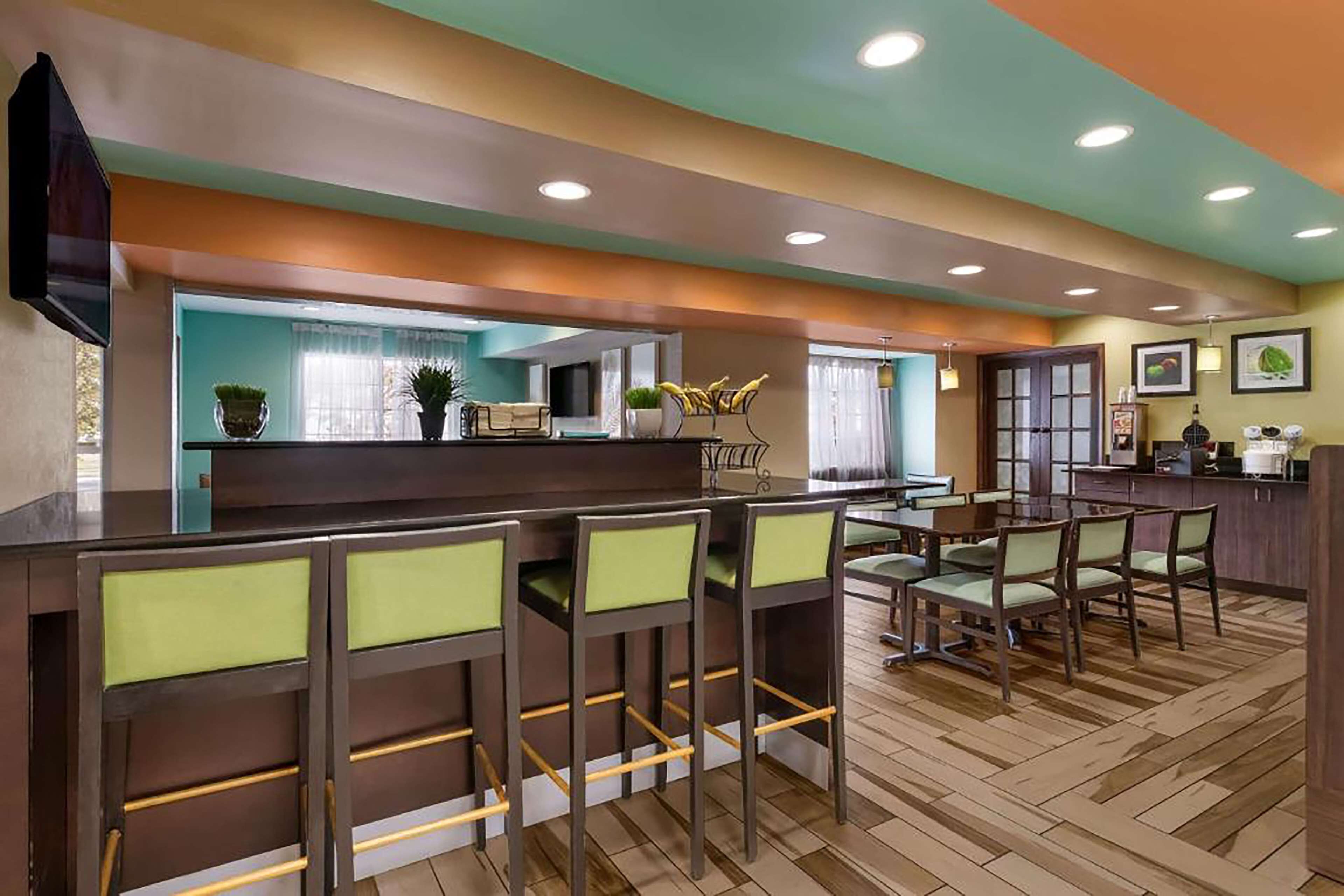 A modern kitchen with a bar area, wooden flooring, and green chairs.