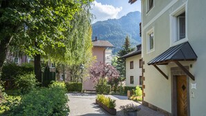 A narrow cobblestone street flanked by buildings with traditional architecture, a bench, and a variety of plants.