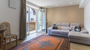 A living room with a sofa, a patterned rug, a chair, and a sliding glass door leading to an outdoor area.