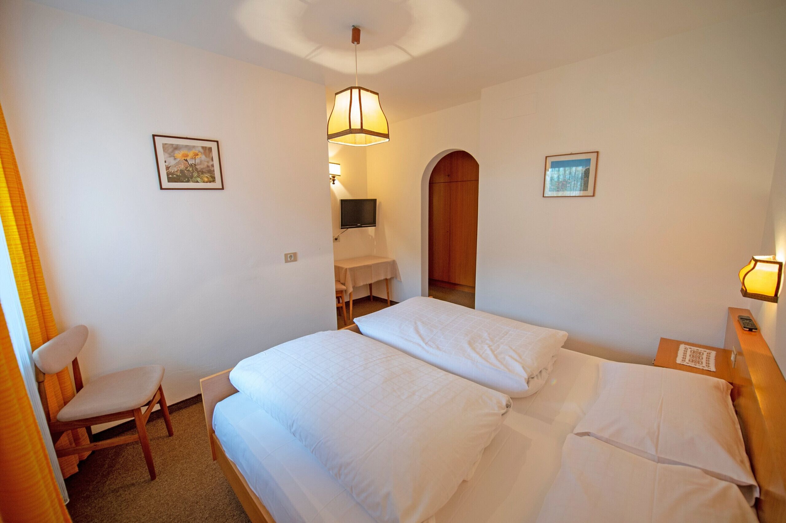 A hotel room with two beds, a chair, a desk, and a TV.