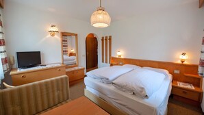 Een hotelkamer met een bed, een bureau met een computer, een stoel, een houten dressoir en een spiegel.