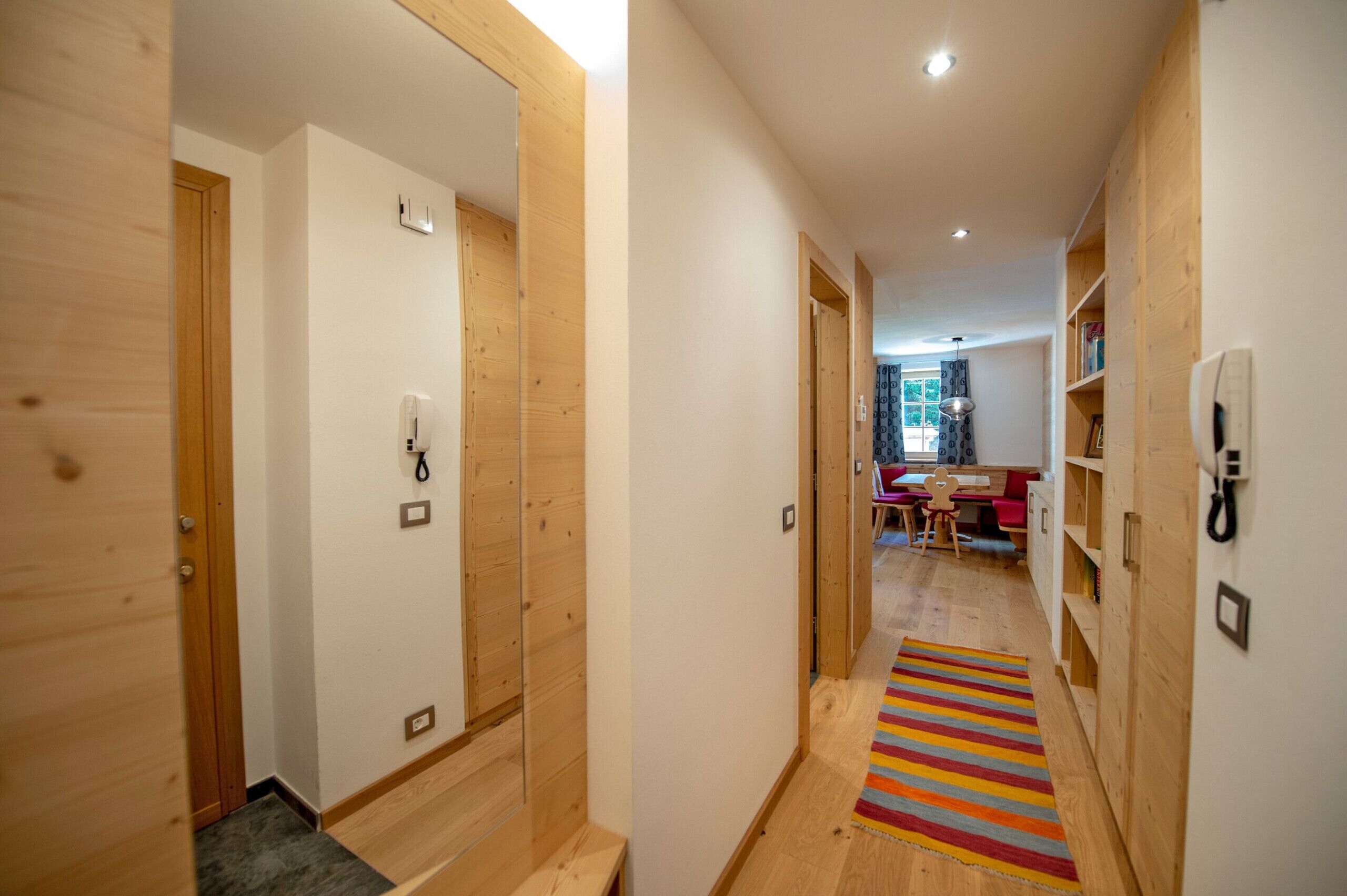 A hallway with wooden walls and doors, a striped rug, and a dining area in the background.