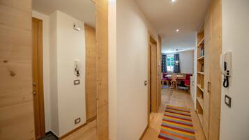 A hallway with wooden walls and doors, a striped rug, and a dining area in the background.