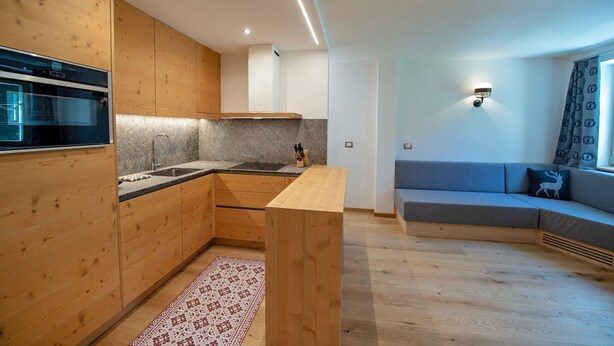 Une cuisine moderne avec des meubles en bois, un four encastré et un plan de travail gris. Le salon est doté d’un canapé gris agrémenté d’un coussin à motifs.