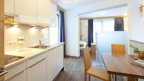 Una cocina moderna con armarios blancos, un lavamanos y una zona de comedor con mesa y sillas de madera.