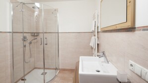 Un baño moderno con ducha de vidrio, lavamanos blanco y tocador de madera.
