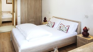 Ein Schlafzimmer mit einem hölzernen Bett, weißer Bettwäsche, einem Nachttisch mit einer Vase und einem Kleiderschrank.