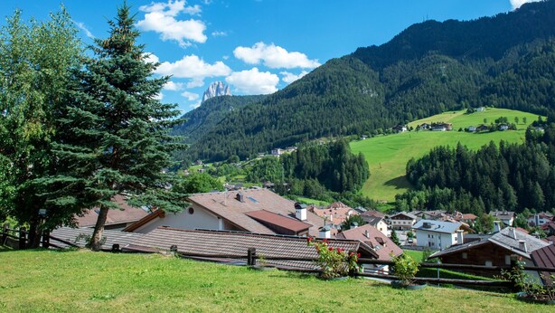 Ein ländliches Dorf mit traditionellen Häusern, einem markanten Berg und einem strahlend blauen Himmel.