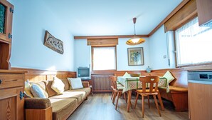 Een gezellige kamer met een houten bank, een eettafel met stoelen, een televisie en een raam met gordijnen.