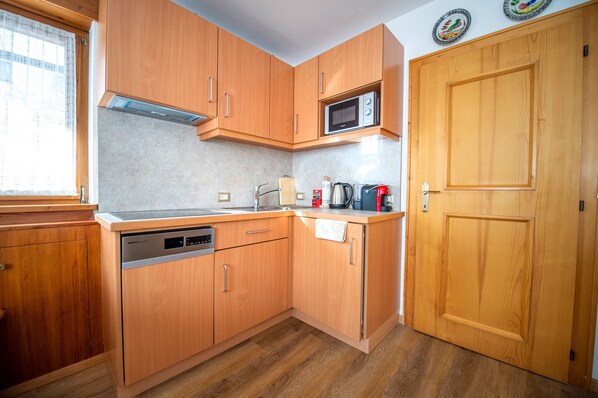 A compact kitchen with wooden cabinets, a built-in microwave, a dishwasher, and a coffee maker.
