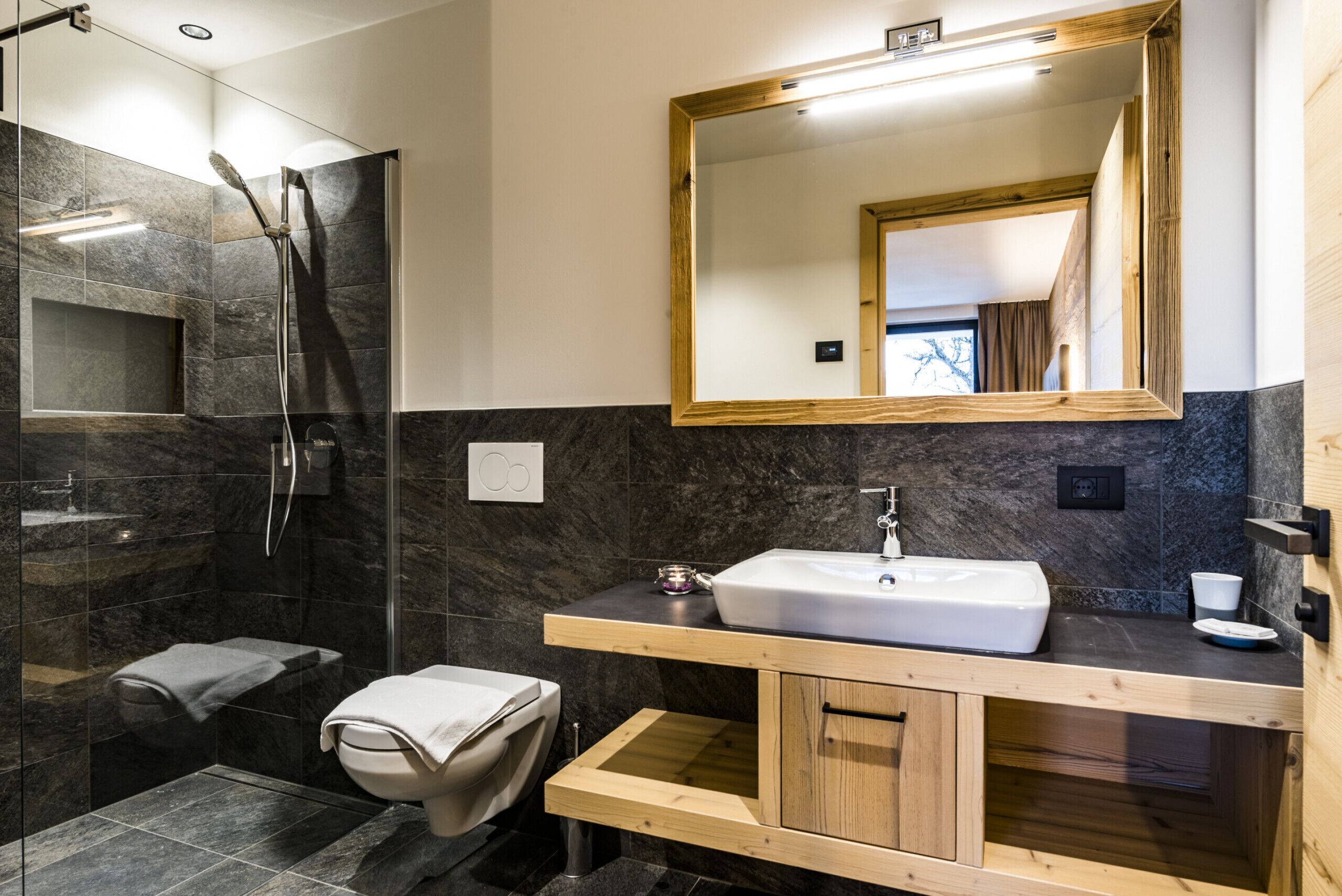 Ein modernes Badezimmer mit einer gläsernen Duschkabine, einem hölzernen Waschtisch mit Waschbecken und einem großen Spiegel.