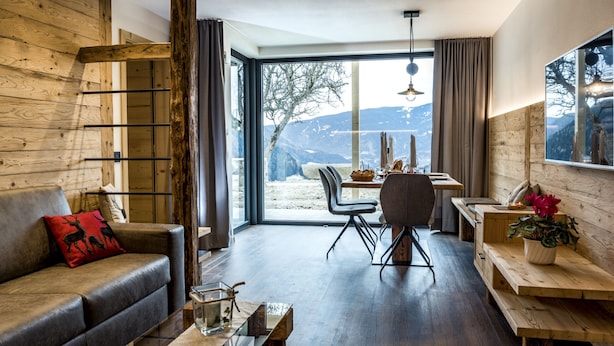 Un salon moderne avec un intérieur en bois, une porte en verre donnant sur un espace repas et une vue sur les montagnes.