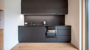 A compact kitchen with dark cabinetry, a built-in oven, and a stainless steel kettle. - Apartments Villa Mayr 125A (Ortisei)