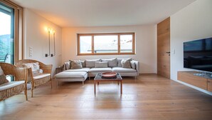 A modern living room with a sectional sofa, a wicker chair, a coffee table, and a TV on a wooden cabinet. - Apartments Villa Mayr 125A (Ortisei)