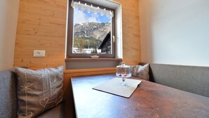 A wooden-paneled room with a window overlooking a mountainous landscape. There is a table with a glass dome centerpiece and a cushion with heart designs. - Apartments Nogler Frieda 124A (Selva di Val Gardena)