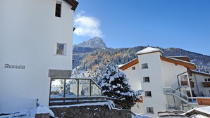A snow-covered building with a mountain view, a wooden bench, and a stone wall. - Apartments Nogler Frieda 124A (Selva di Val Gardena)