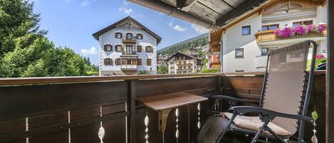 A balcony with a wooden table and chair, overlooking a town with traditional buildings.