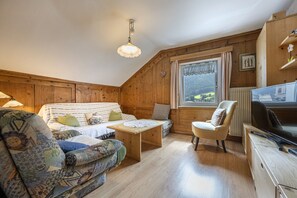 A cozy room with a wooden interior, a sofa, a chair, a small table, and a television.