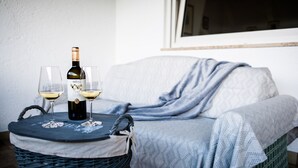 A wicker table with a bottle of wine and two glasses on a blue mat, placed on a wicker stool next to a bed with a blue blanket. - Apartments Matilde 201A (Fiè allo Sciliar)