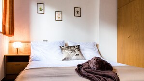 A neatly made bed with white linens, a brown blanket, and a pillow with a deer design. There is a wooden nightstand with a lamp, and a wooden wardrobe to the right. - Apartments Matilde 201A (Fiè allo Sciliar)