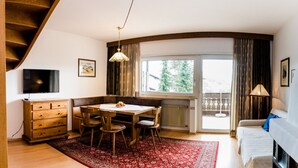 A cozy room with a wooden staircase, a dining table with chairs, a TV, and a large window with curtains. - Apartments Matilde 201A (Fiè allo Sciliar)