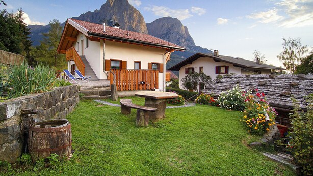 Un chalet rustique doté d’une terrasse en bois, d’une cuve en pierre et d’un jardin fleuri.