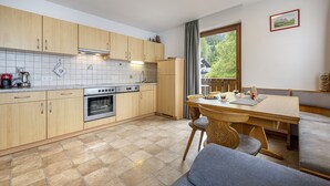 Une cuisine moderne avec des meubles en bois, un four encastré et un coin repas comprenant une table et des chaises en bois.