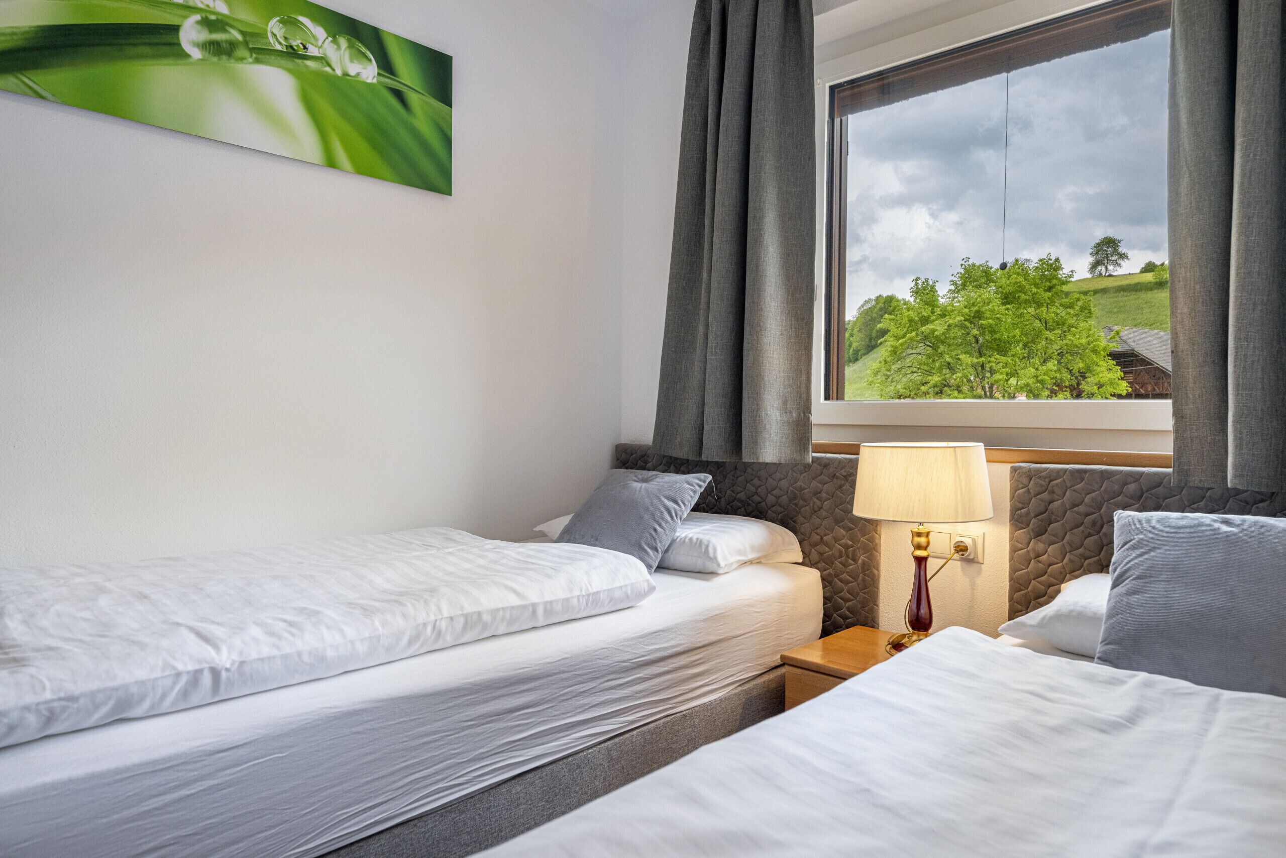 Une chambre d’hôtel avec deux lits, une fenêtre donnant sur des arbres et une lampe sur la table de chevet.