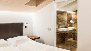 Moderni hotellihuone, jossa on sänky, yöpöytä ja kylpyhuone, jossa on marmoriseinä ja kaksi pesuallasta.