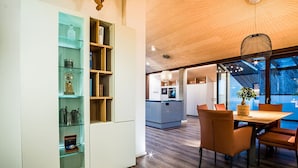 Een moderne keuken met een houten plafond, een eethoek met oranje stoelen en een glazen kast met diverse spullen.