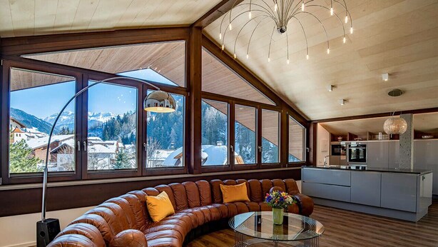 Een moderne woonkamer met een gebogen leren bank, een glazen salontafel en grote ramen met uitzicht op een besneeuwd berglandschap.