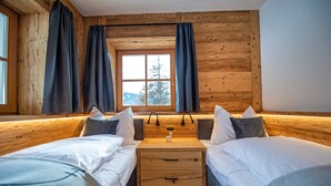 A room with two beds, wooden walls, a window with curtains, and a small table with a decorative item.