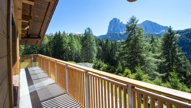 A wooden balcony with a view of a forest and mountains.