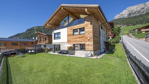 Ein modernes, zweistöckiges Haus mit geneigtem Dach, großen Fenstern und einem gepflegten Rasen.