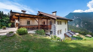 Una baita a due piani con un balcone, travi in legno e uno sfondo montano.