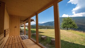 A wooden cabin with large windows offering a view of a grassy field and mountains. - Residence Chalet Alpina 143E (Ortisei)