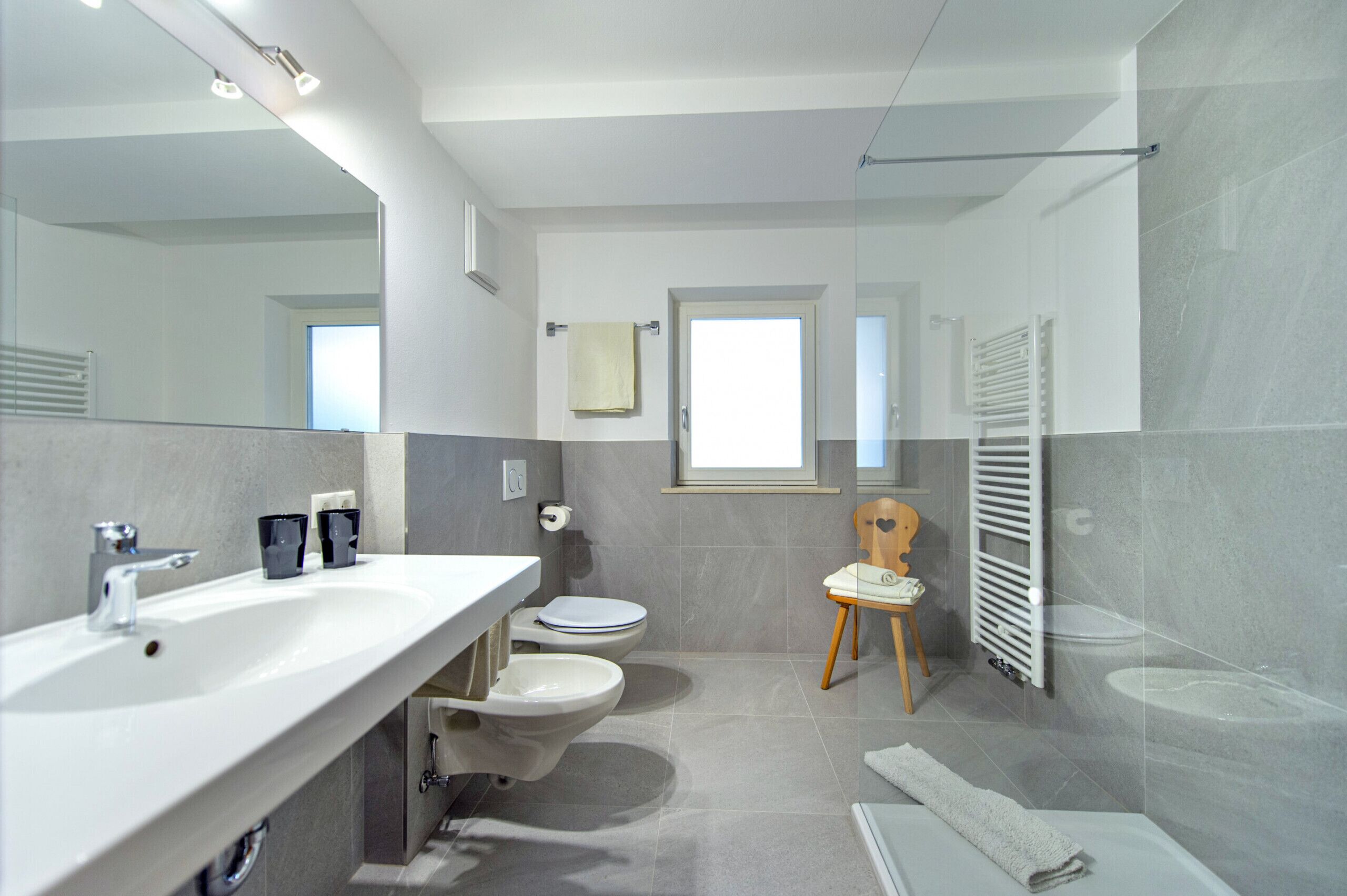 Une salle de bain moderne avec un grand miroir, un lavabo blanc, deux toilettes, un espace douche et un porte-serviettes.