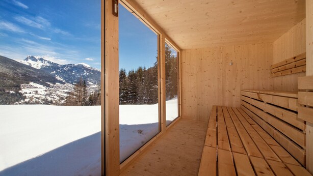 Una cabaña de madera con amplias ventanas que ofrecen vistas a montañas nevadas.