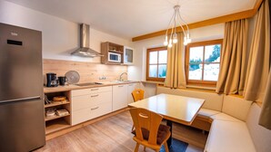 A compact kitchen with a refrigerator, microwave, and wooden cabinets. There's a dining table with chairs and a built-in bench. - Residence Chalet Alpina 143C (Ortisei)