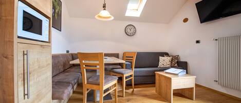 A compact living space with a dining area, a sofa, a TV mounted on the wall, and a clock.