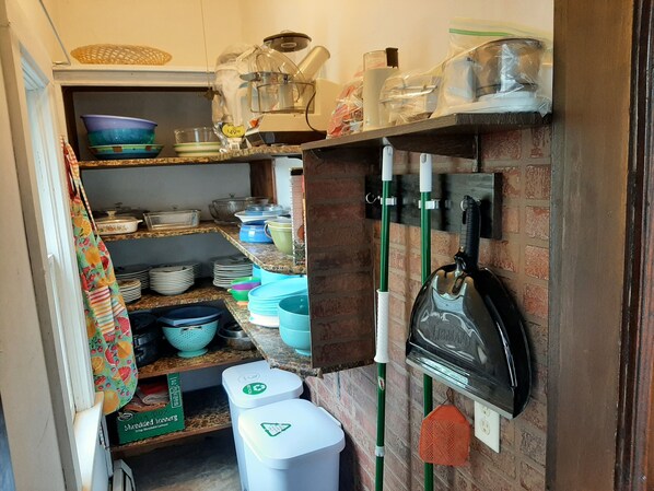 A narrow kitchen with shelves holding various dishes, a kettle, and a trash bin. - Charming Cottage in Stockholm, WI
Nations Best: Pies, Scenic Drive, Small Town! (Stockholm)