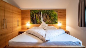 Ein Schlafzimmer mit einem hölzernen Bett, zwei Nachttischen, einem großflächigen Wandbild mit Waldmotiv und zwei Wandlampen.