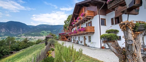 A traditional chalet with wooden balconies, a gravel pathway, and a view of a valley.
