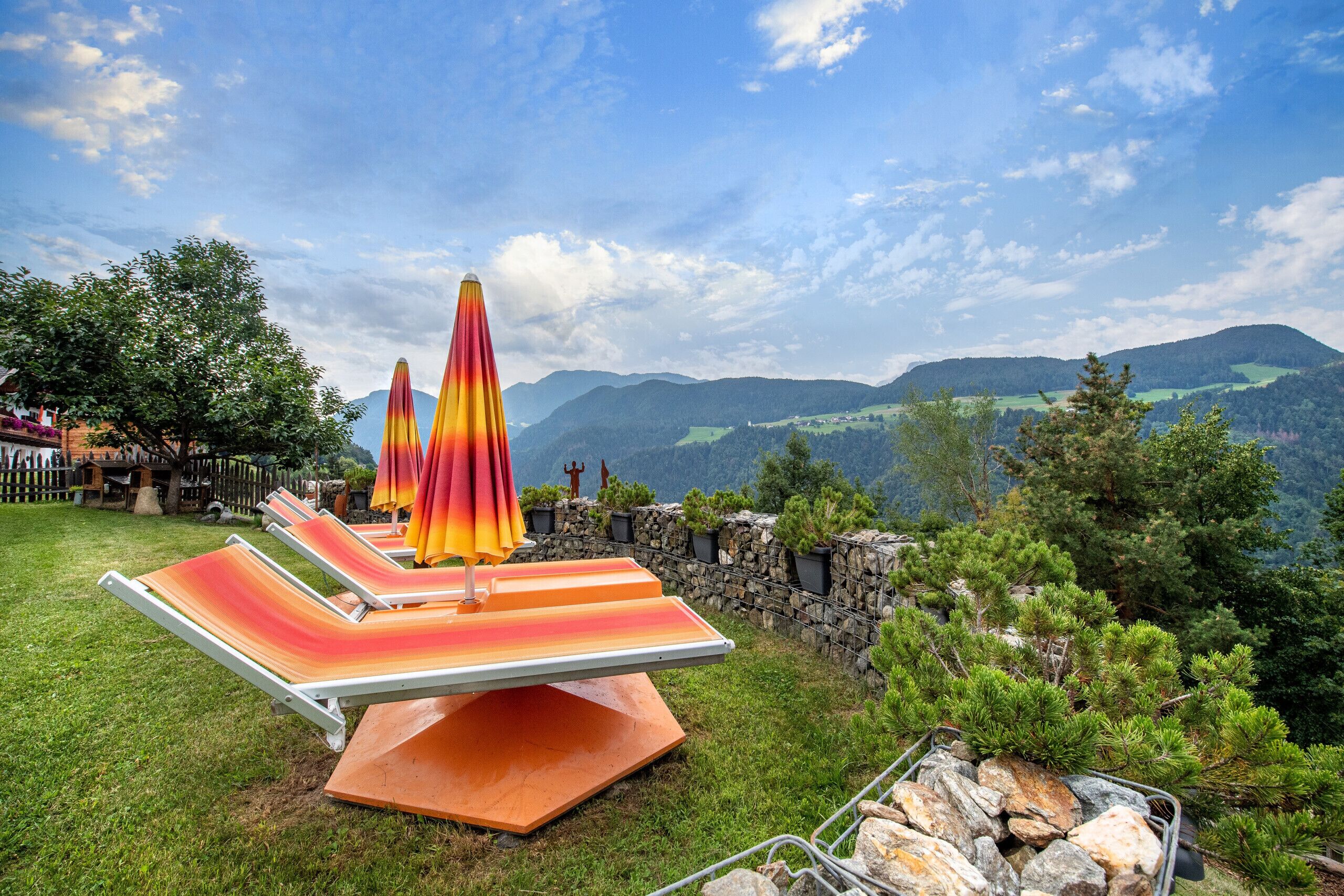 Terraço com cadeiras de estar e guarda-sóis, com vista para uma paisagem montanhosa.