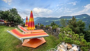 Une terrasse dotée de chaises longues et de parasols, offrant une vue sur un paysage montagneux.
