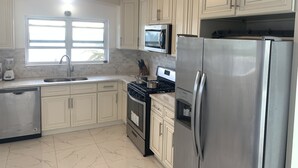 A kitchen with white cabinets, stainless steel appliances, a microwave, a refrigerator, a stove, and a window with natural light.
