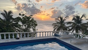 A swimming pool with a view of the ocean and palm trees at sunset.