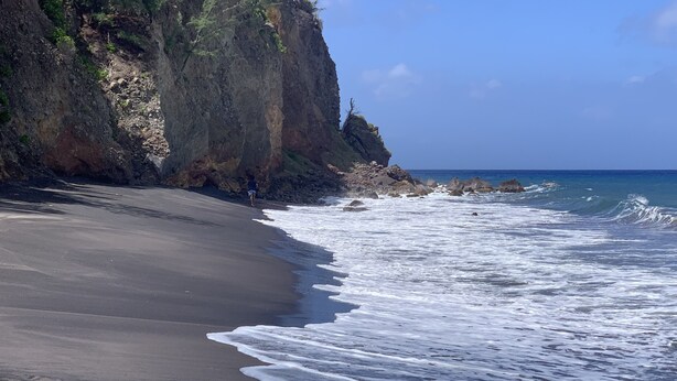 A beach with a rocky cliff and waves crashing onto the shore.