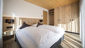 Een moderne slaapkamer met een houten plafond, een groot bed met witte lakens, een televisie aan de muur en een houten kledingkast.